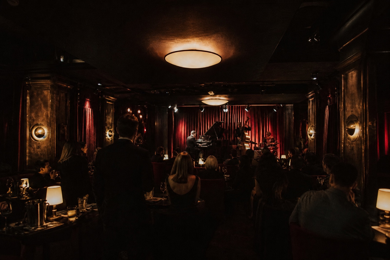 Dunkle Lounge mit weinroten Vorhängen, gedämpftes Licht, Gäste an Tischen